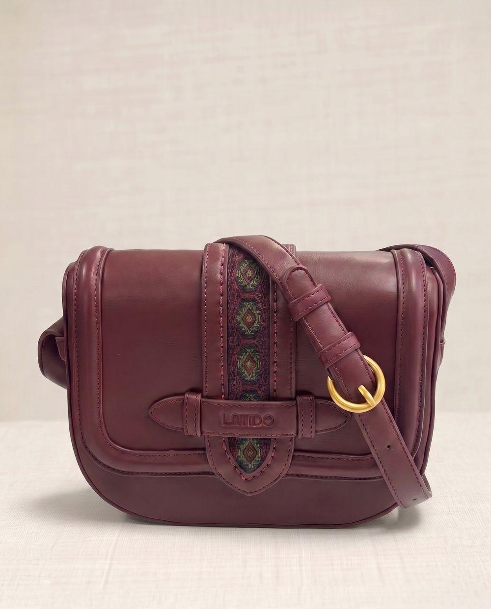 a maroon leather bag with a gold ring on the strap