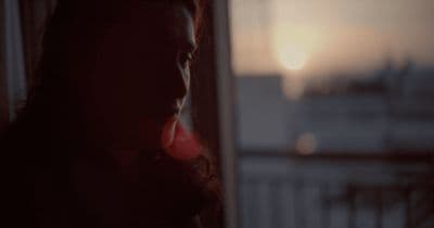 a woman standing in front of a window at sunset