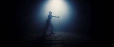 a man standing in the dark with his arms outstretched