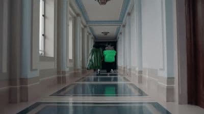 a man in a green jacket walking down a hallway