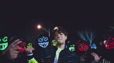 a man standing in front of a group of people wearing neon masks