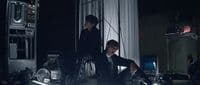 a man in a suit sitting on a chair next to another man in a suit