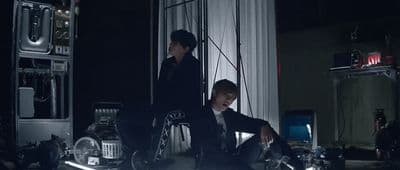 a man in a suit sitting on a chair next to another man in a suit