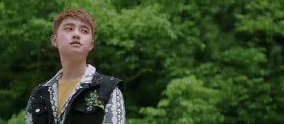 a young man standing in front of a lush green forest