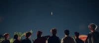 a group of people watching a kite fly in the sky