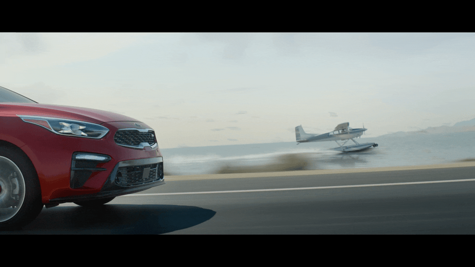 a red car driving down a road next to an airplane