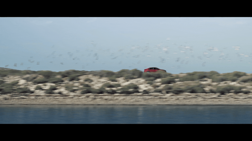 a red car driving down a road next to a body of water