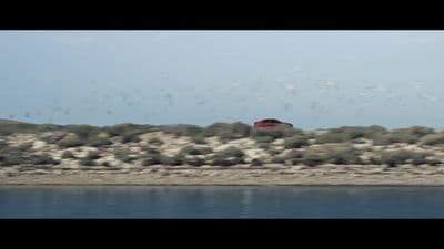 a red car driving down a road next to a body of water