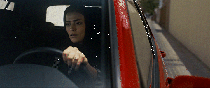 a woman driving a red car down a street