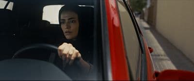 a woman driving a red car down a street