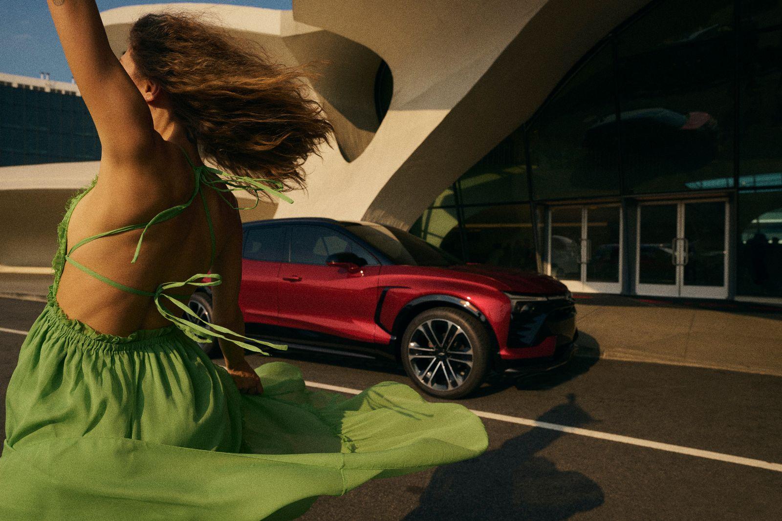 a woman in a green dress dancing in front of a red sports car