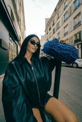 a woman in a black leather jacket and sunglasses sitting on a scooter