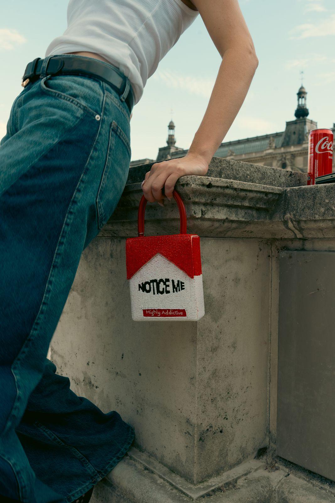a person leaning on a wall holding a red and white bag