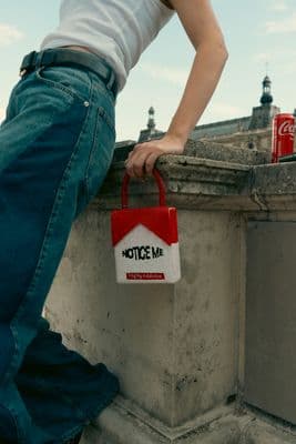 a person leaning on a wall holding a red and white bag