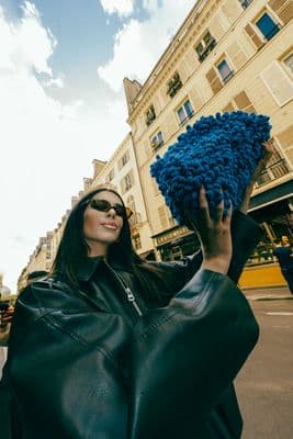a woman in a black leather jacket holding a blue pom - pom