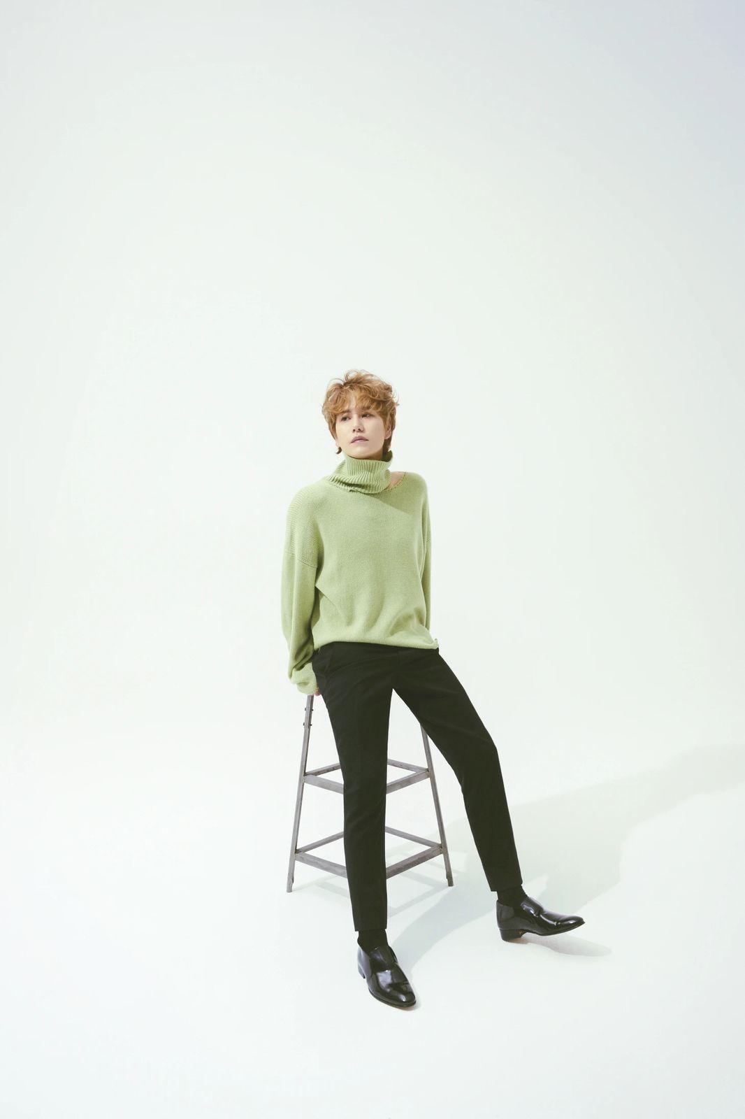 a woman sitting on a stool wearing a green sweater