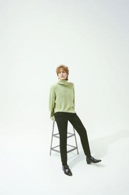 a woman sitting on a stool wearing a green sweater