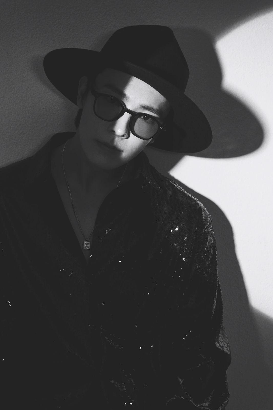 a man wearing a hat and glasses standing against a wall