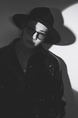 a man wearing a hat and glasses standing against a wall