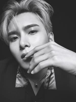 a man in a black shirt and tie with his hand on his face