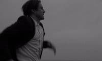 a man in a suit and tie running on the beach