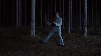 a man in a suit is walking through the woods