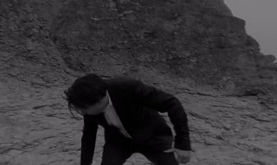 a man in a suit and tie standing on a rocky hill
