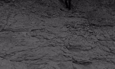 a black and white photo of a man standing on a rocky hill