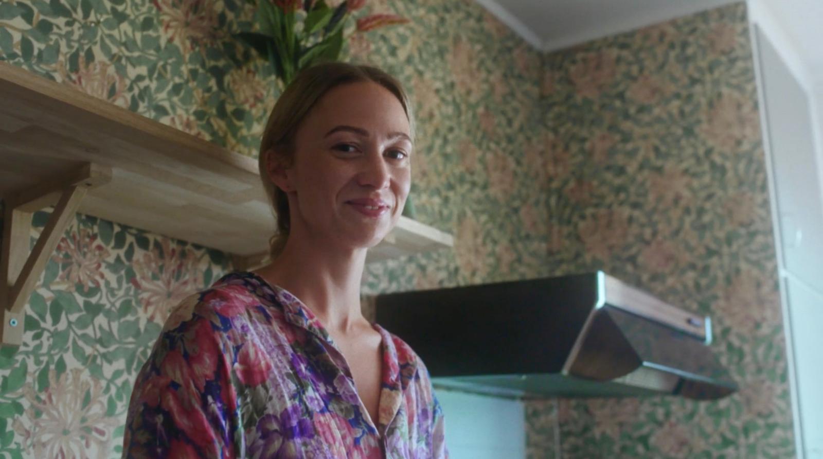a woman in a floral shirt standing in front of a kitchen