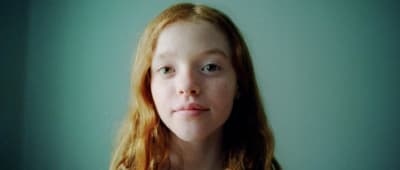 a young girl with red hair is looking at the camera