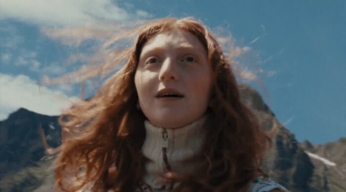 a woman with red hair standing in front of a mountain