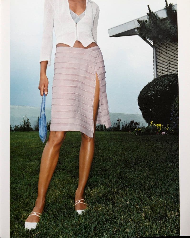 a woman standing in the grass wearing a skirt