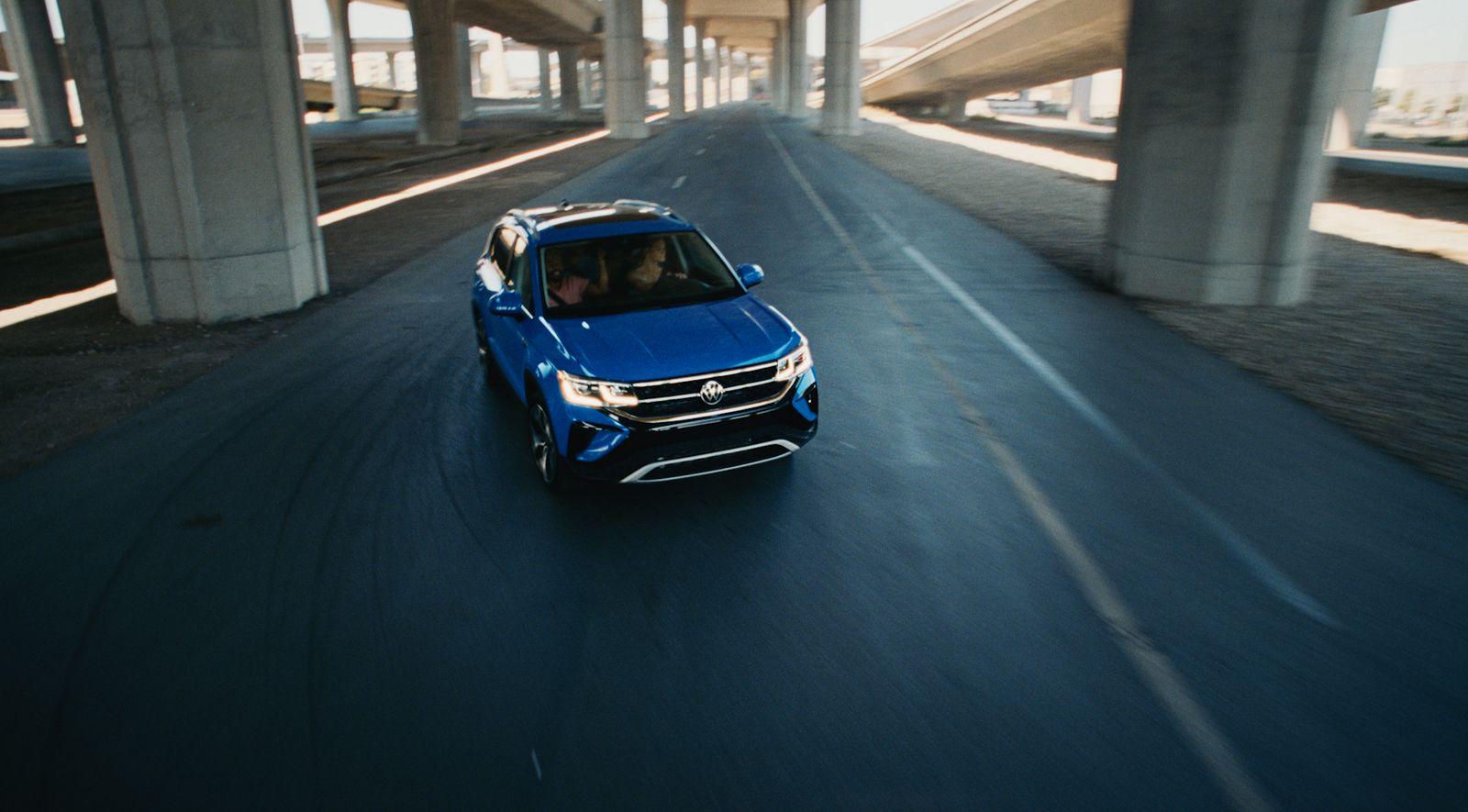 a blue car driving down a highway under a bridge