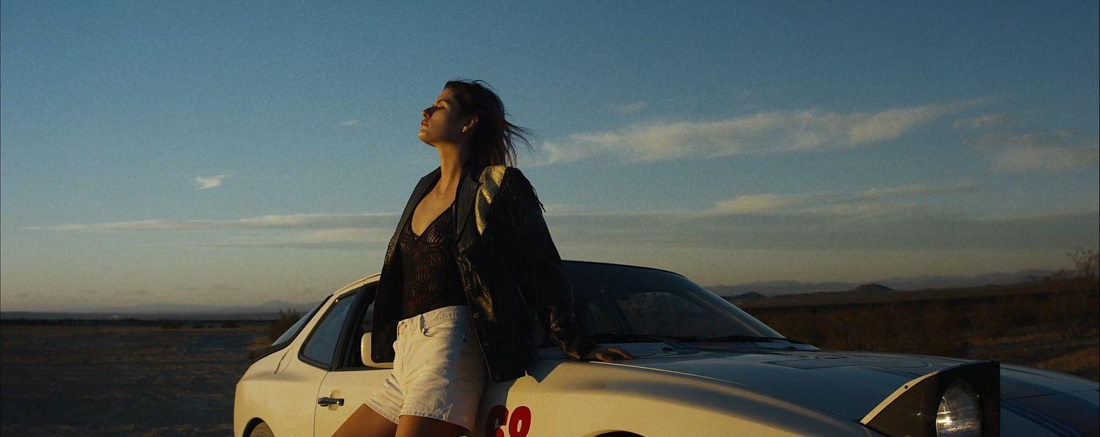 a woman leaning on the hood of a car