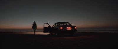 a person standing next to a car on a beach