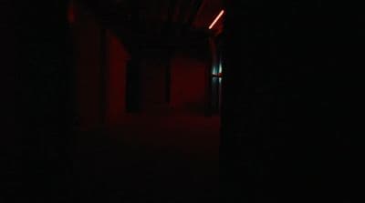 a dark hallway with a red light at the end of it