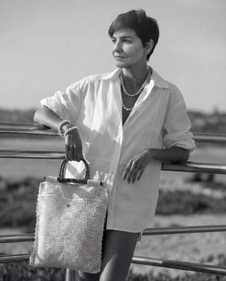 a woman holding a purse standing next to a fence