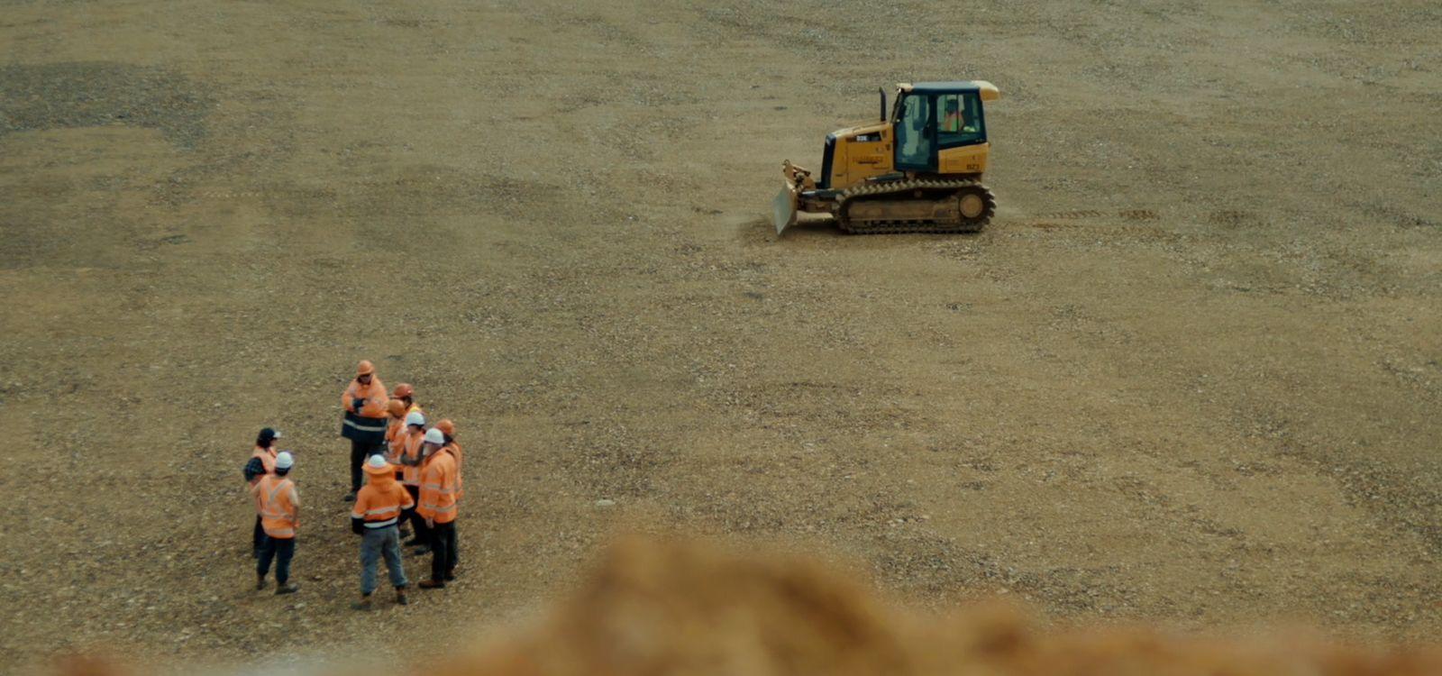 a group of people in orange vests standing in front of a bulldozer