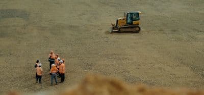 a group of people in orange vests standing in front of a bulldozer