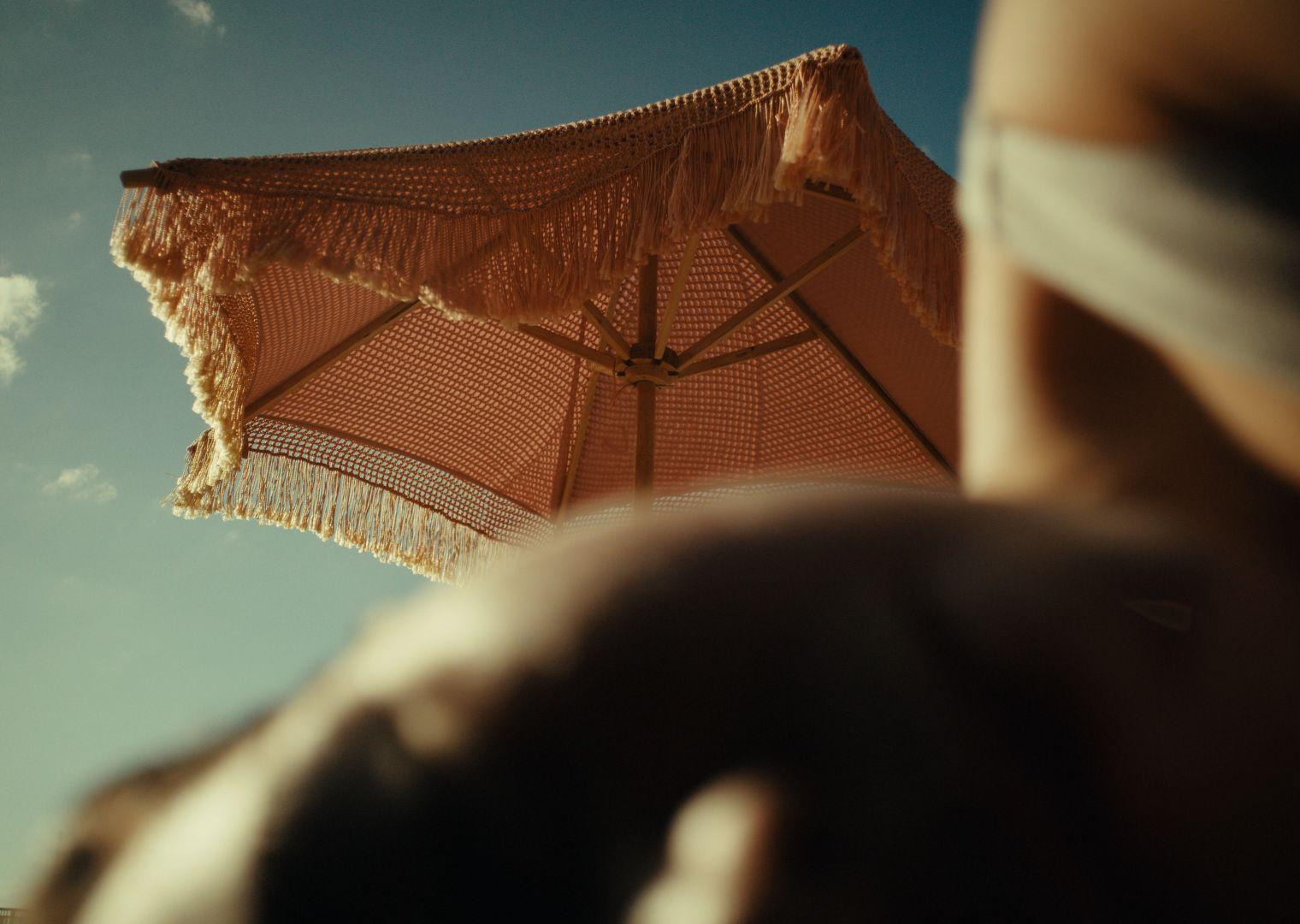 a person holding a brown umbrella under a blue sky
