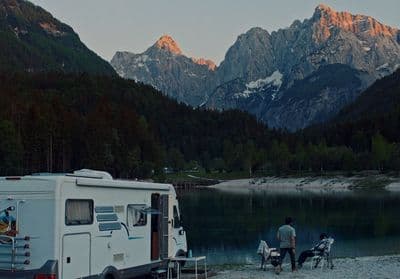 a camper parked next to a lake with mountains in the background
