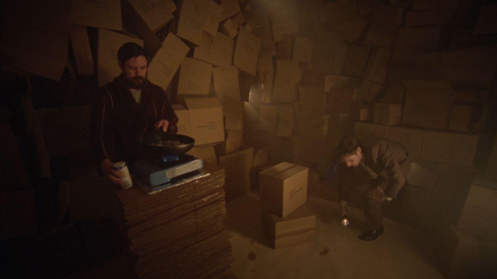two men in a dark room with stacks of boxes