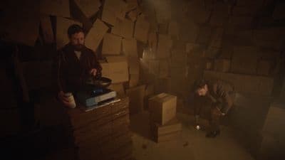 two men in a dark room with stacks of boxes