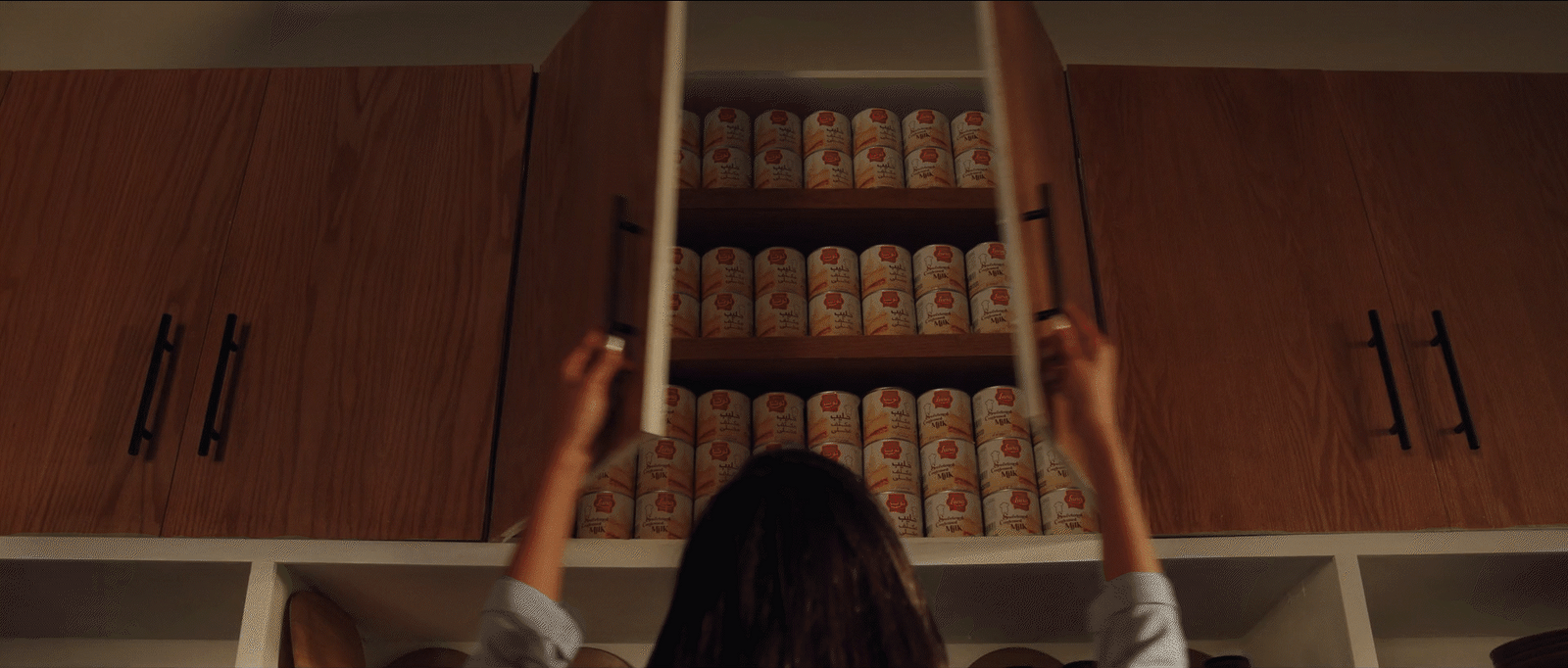 a woman reaching up to reach a shelf full of canned food