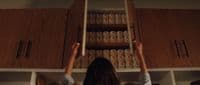 a woman reaching up to reach a shelf full of canned food