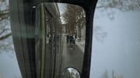 a rear view mirror on a vehicle reflecting people on the street
