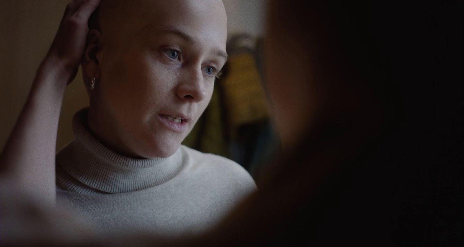 a woman with a bald head is looking in the mirror