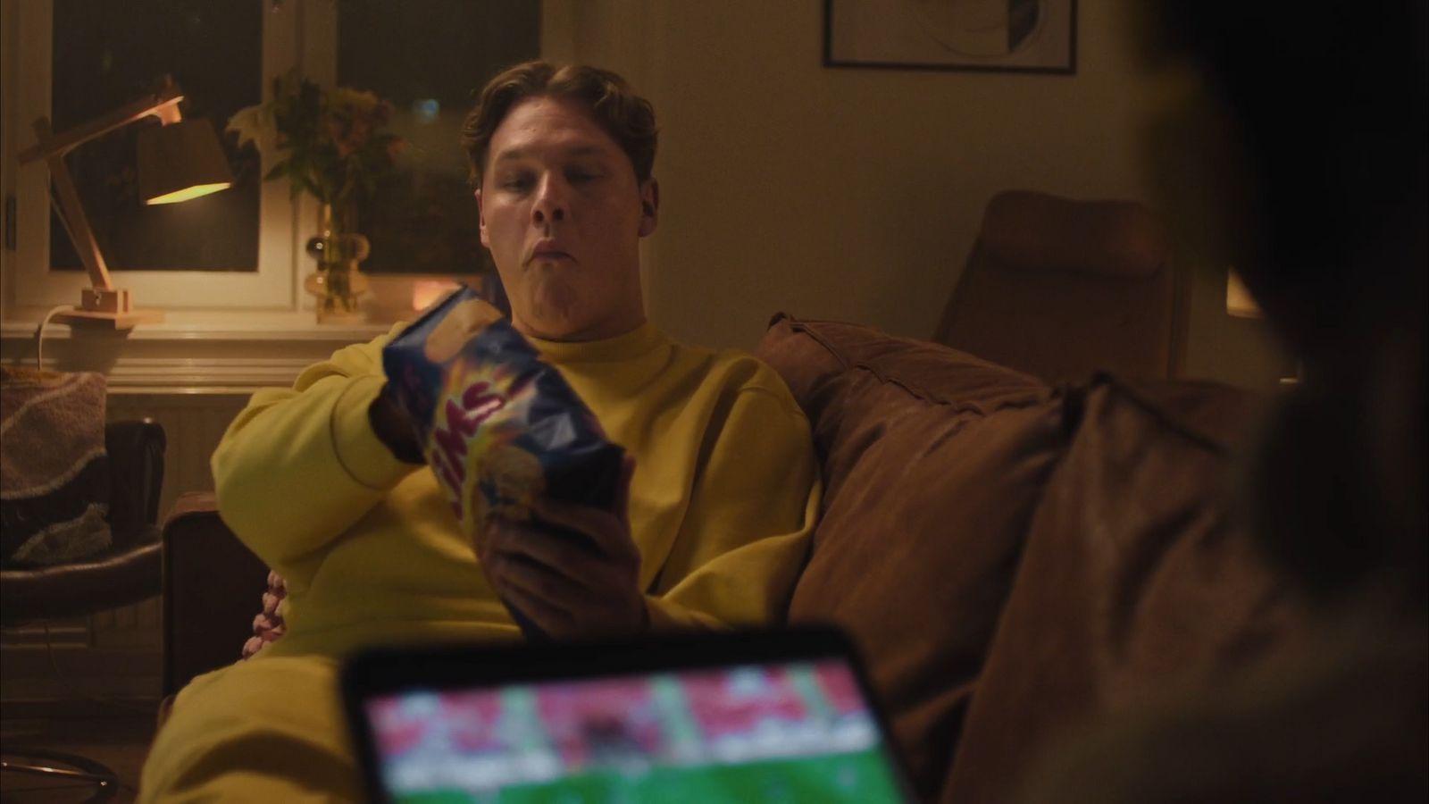 a man sitting on a couch holding a box of chips