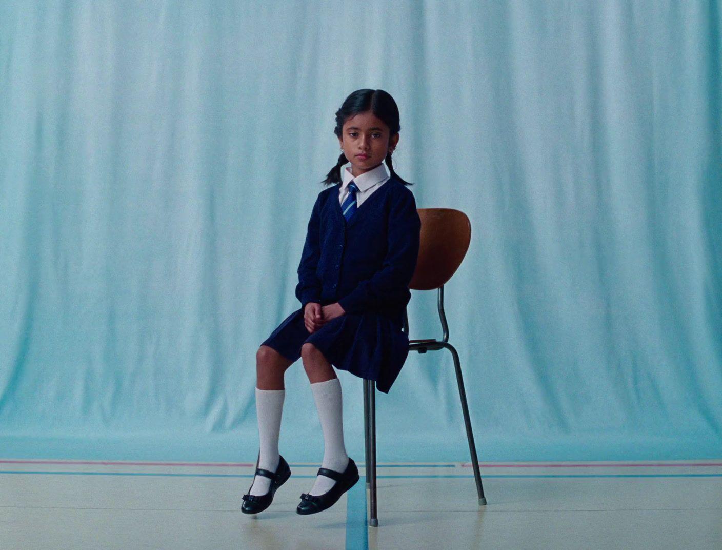 a young girl sitting on a chair in front of a blue backdrop