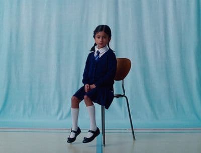 a young girl sitting on a chair in front of a blue backdrop